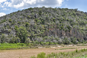 A muddy Colorado River flows past cliff-rimmed hills of Ellenburger dolomite